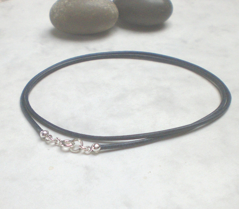 May include: A dark blue leather cord necklace with a silver clasp and two silver beads.