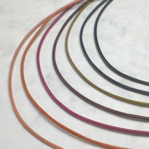 May include: A set of seven leather cords in various colors, including peach, orange, pink, burgundy, brown, olive green, and navy blue. The cords are arranged in a semi-circle, with the lightest color at the top and the darkest color at the bottom.