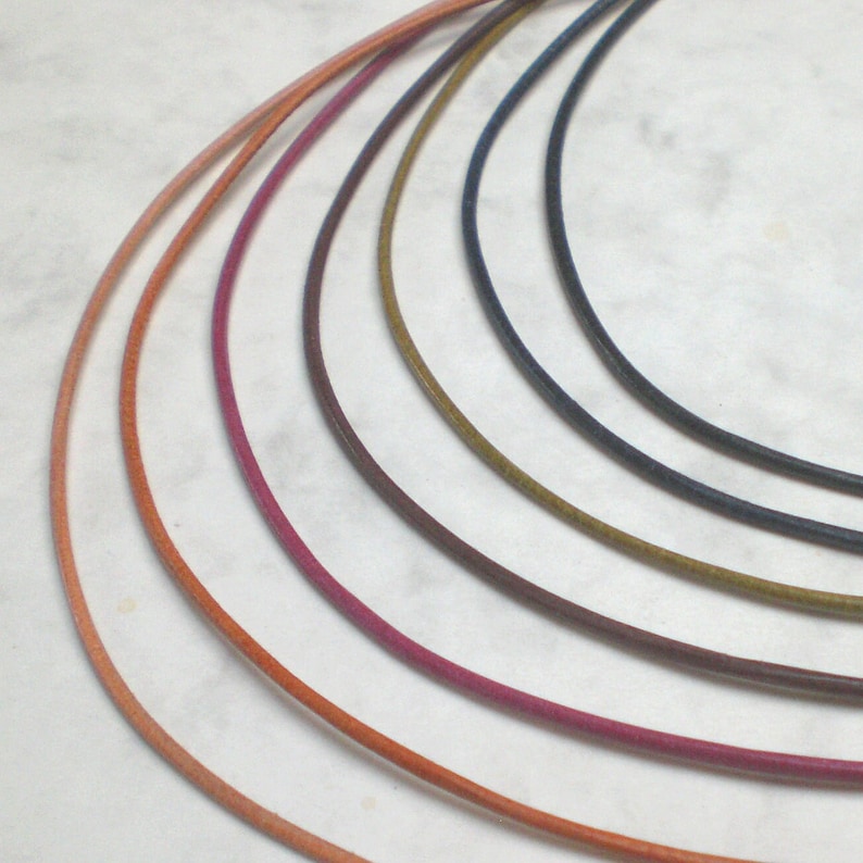 May include: A set of seven leather cords in various colors, including peach, orange, pink, burgundy, brown, olive green, and navy blue. The cords are arranged in a semi-circle, with the lightest color at the top and the darkest color at the bottom.