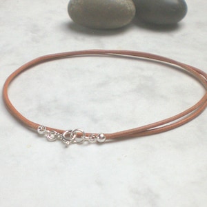 May include: A brown leather cord necklace with a silver clasp and two silver beads.