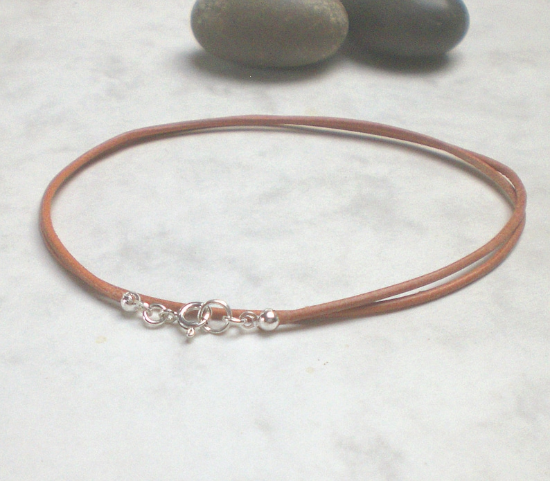 May include: A brown leather cord necklace with a silver clasp and two silver beads.