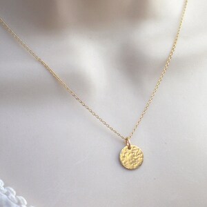 May include: A delicate gold chain necklace with a hammered, circular pendant.