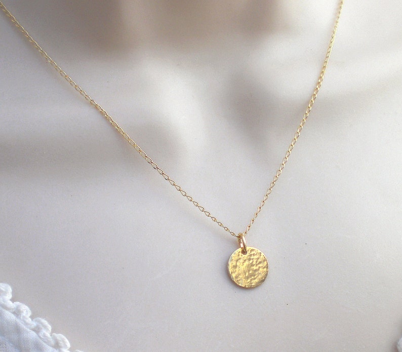 May include: A delicate gold chain necklace with a hammered, circular pendant.