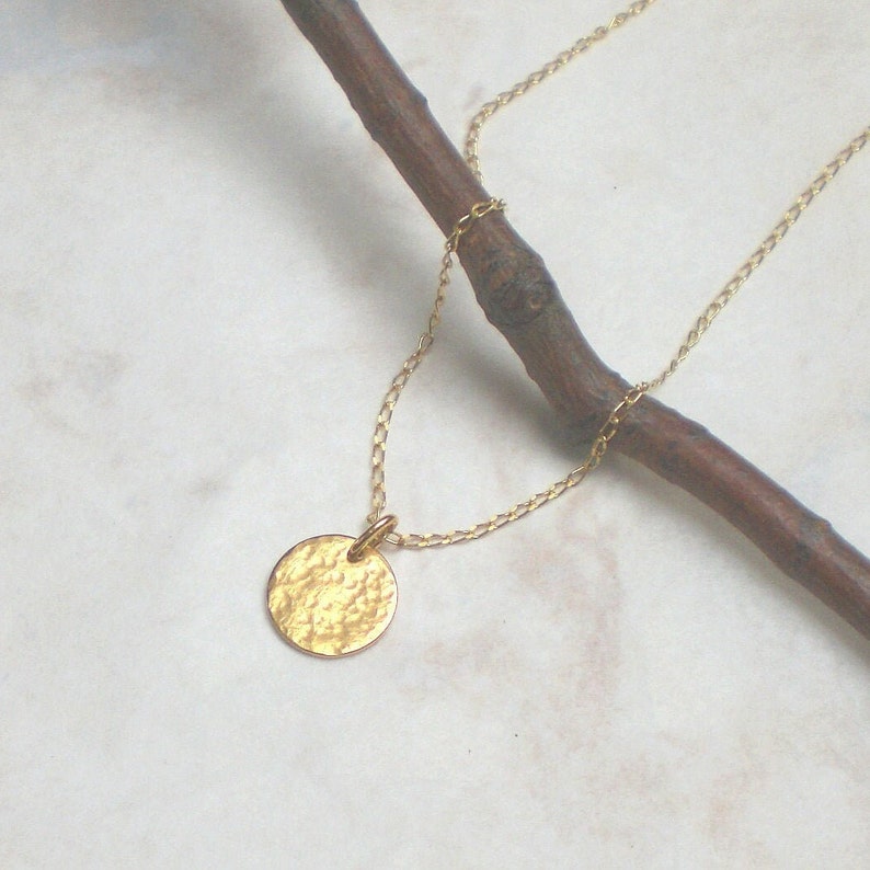 May include: A gold chain necklace with a hammered gold circle pendant.
