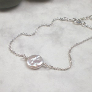 May include: A delicate silver chain necklace with a single, large, white pearl pendant.
