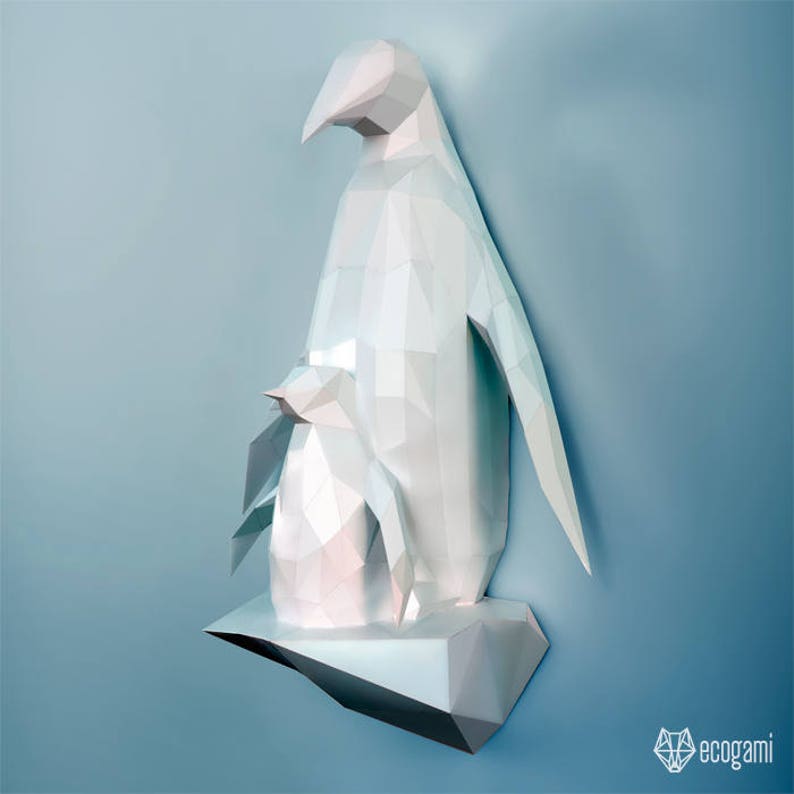May include: A white papercraft penguin sculpture with a smaller penguin nestled on its back. The penguins are standing on a white papercraft iceberg.