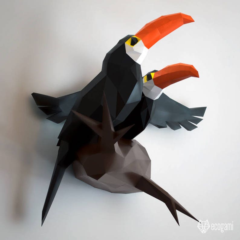 May include: Two origami toucans perched on a brown branch. The toucans are made of black, white, and orange paper. The toucans are facing different directions. The toucans are made of paper and are a 3D origami sculpture.