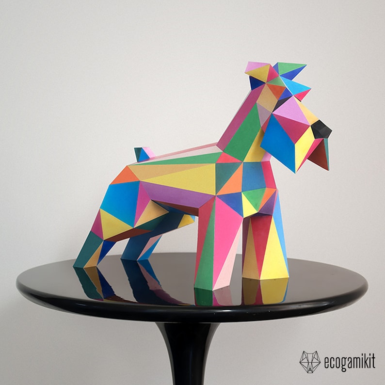 K&ouml;nnte beinhalten: Ein farbenfrohes Papiermodell eines Hundes, hergestellt aus geometrischen Formen in den Farben Rosa, Blau, Gr&uuml;n, Gelb und Rot. Der Hund steht auf einem schwarzen Tisch, auf dessen Oberfl&auml;che sich der Hund spiegelt.