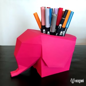 Peut inclure: Un porte-crayons en forme d'éléphant en origami rose avec une variété de marqueurs colorés à l'intérieur.
