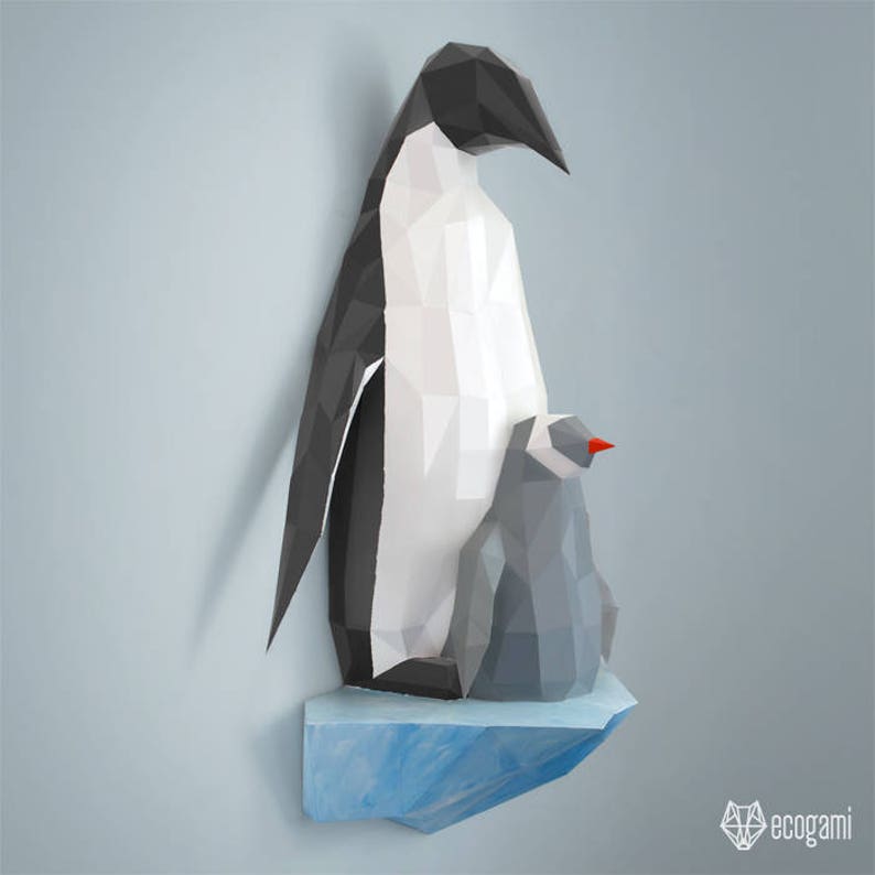 May include: A papercraft penguin sculpture with a smaller penguin chick nestled on its back. The penguins are made of white and black paper and are standing on a blue paper ice shelf. The sculpture is a 3D model and is a great example of papercraft art.
