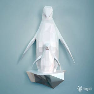 May include: A white papercraft penguin family with a larger penguin standing on a smaller penguin, both standing on a white papercraft iceberg. The penguins are made of folded paper and have a geometric design.