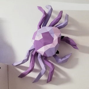 May include: A purple and lavender papercraft crab with a geometric design. The crab is made of folded paper and has a three-dimensional appearance.