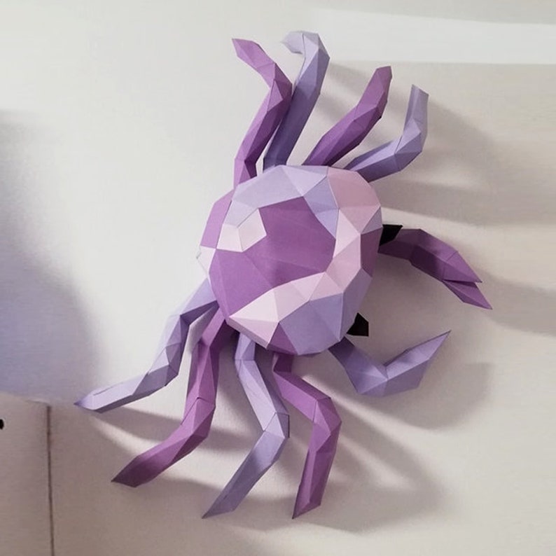 May include: A purple and lavender papercraft crab with a geometric design. The crab is made of folded paper and has a three-dimensional appearance.