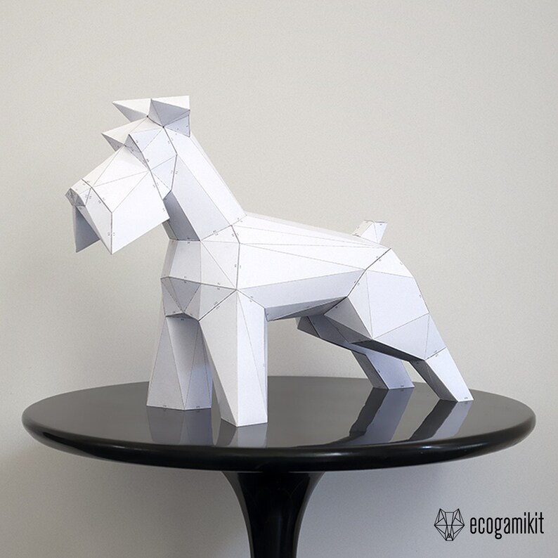 K&ouml;nnte beinhalten: Ein wei&szlig;es Papiermodell eines Schnauzer-Hundes, das auf einem schwarzen Tisch steht. Das Modell besteht aus gefaltetem Papier und hat ein geometrisches Design.
