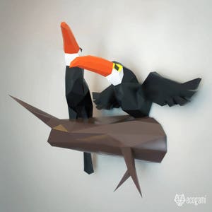 May include: Two toucans perched on a brown tree branch. The toucans are made of paper and have a 3D origami style. The toucans are black with orange beaks and yellow accents.