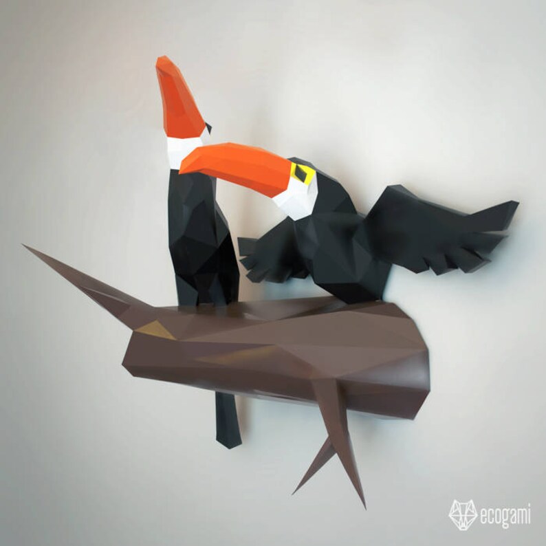 May include: Two toucans perched on a brown tree branch. The toucans are made of paper and have a 3D origami style. The toucans are black with orange beaks and yellow accents.