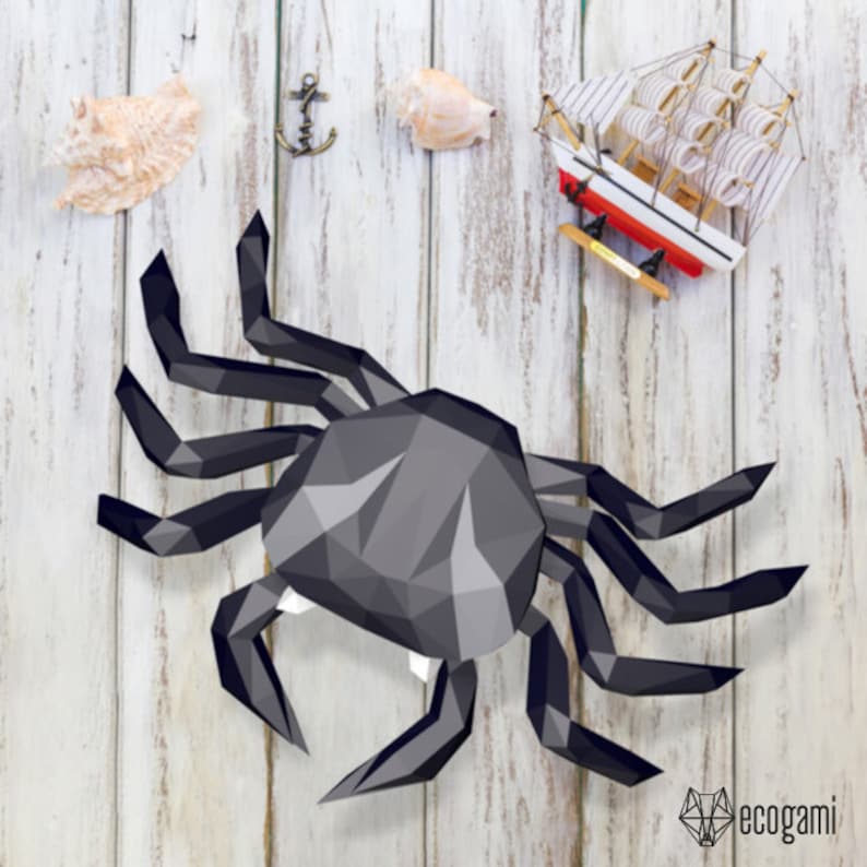 May include: A black papercraft crab with a detailed, geometric design. The crab is posed with its legs outstretched, as if it is walking. The crab is on a white wooden background.
