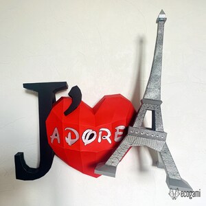 May include: A red paper heart with the word "J'ADORE" written on it, a black paper letter "J", and a gray paper model of the Eiffel Tower.