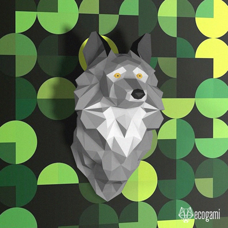 Peut inclure: Une t&ecirc;te de loup en papiercraft grise avec des yeux jaunes sur un fond g&eacute;om&eacute;trique vert et noir.