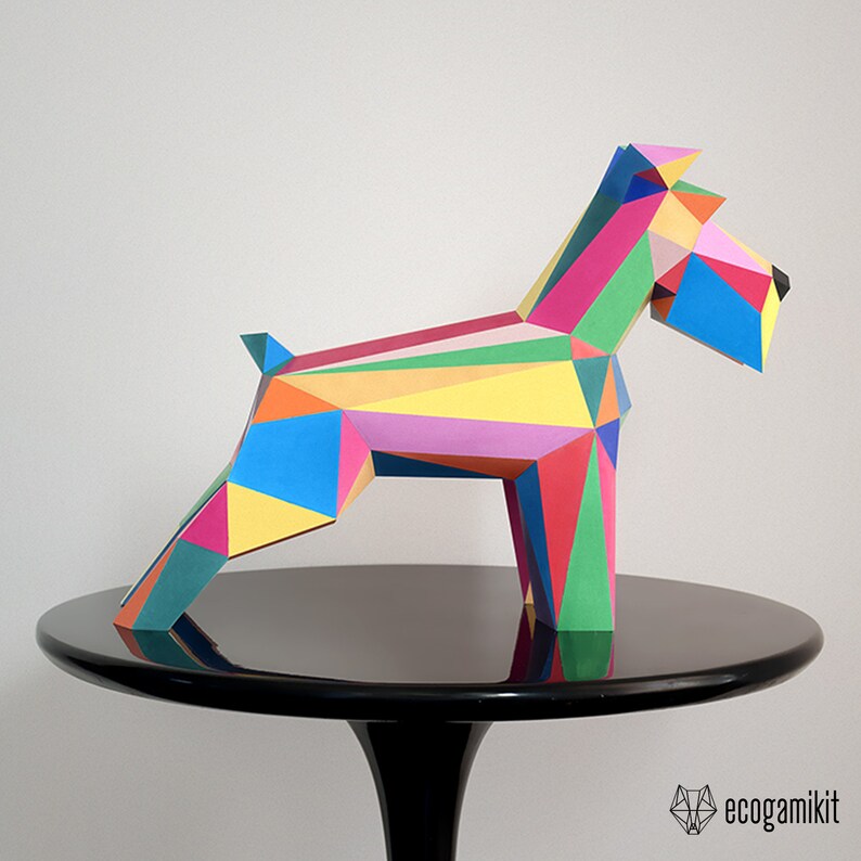 K&ouml;nnte beinhalten: Ein farbenfrohes Papiermodell eines Hundes, hergestellt aus geometrischen Formen. Der Hund steht auf einem schwarzen Tisch mit wei&szlig;em Hintergrund. Der Hund ist aus Papier gefertigt und in verschiedenen Farben bemalt, darunter Rot, Gelb, Blau, Gr&uuml;n und Pink.