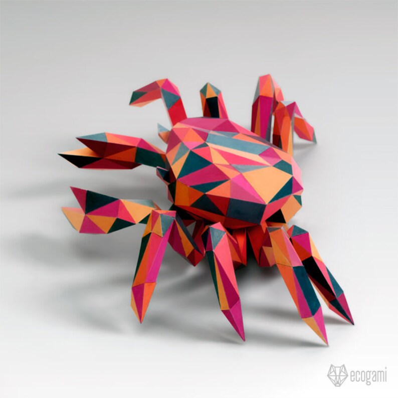 May include: A colorful papercraft spider with a geometric design. The spider is made of red, orange, pink, black, and blue paper. The spider is posed with its legs outstretched.