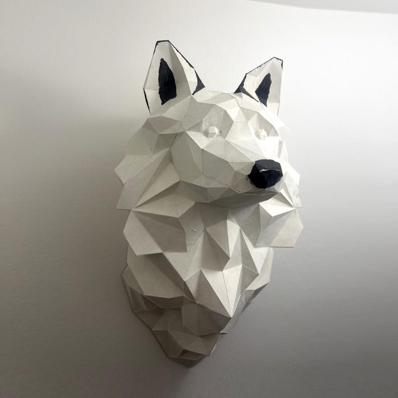 Peut inclure: Une sculpture de t&ecirc;te de loup en papier m&acirc;ch&eacute; blanc avec des oreilles et un nez peints en noir. La sculpture est faite de formes g&eacute;om&eacute;triques et a un effet 3D.
