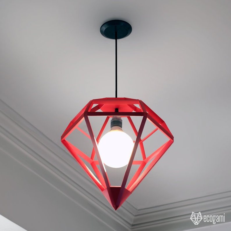 May include: Red diamond-shaped pendant light fixture with a visible light bulb. The geometric design is suspended from a black ceiling mount. The light fixture is a modern home decor item.