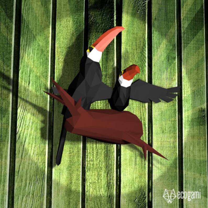 May include: Two origami toucans perched on a brown branch, with a green wooden background. The toucans are black with yellow and red accents.
