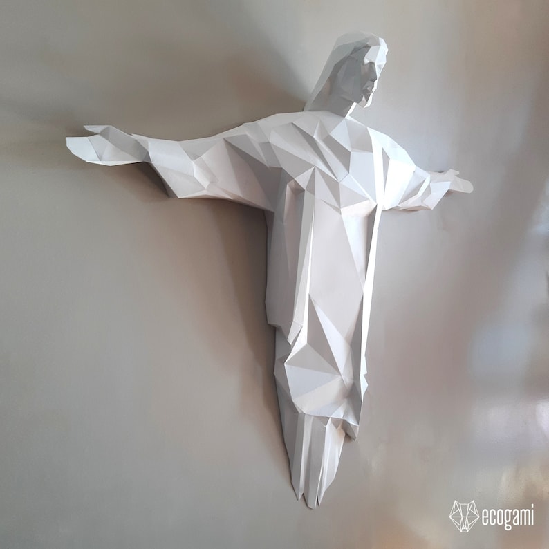 May include: A white paper sculpture of a person with outstretched arms, resembling the famous Christ the Redeemer statue in Rio de Janeiro, Brazil.