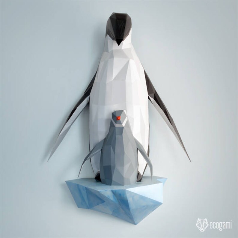 May include: A papercraft penguin family with a larger penguin standing on a smaller penguin. The penguins are made of white, black, and gray paper and are standing on a blue paper iceberg.