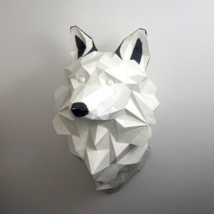 Peut inclure: Sculpture de t&ecirc;te de loup en papier m&acirc;ch&eacute; blanc avec des d&eacute;tails peints en noir. La t&ecirc;te du loup est faite de formes g&eacute;om&eacute;triques et a un effet 3D.