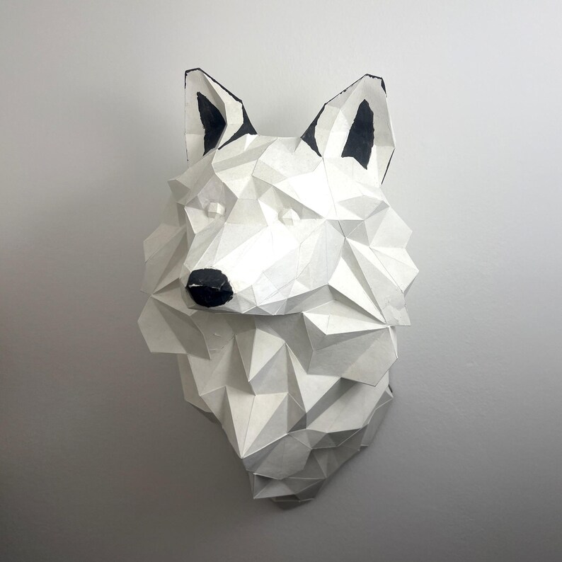 Peut inclure: Sculpture de t&ecirc;te de loup en papier m&acirc;ch&eacute; blanc avec des d&eacute;tails peints en noir. La t&ecirc;te du loup est faite de formes g&eacute;om&eacute;triques et a un effet 3D.