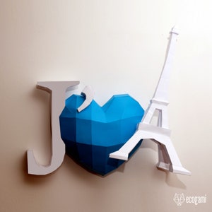 May include: A papercraft model of the Eiffel Tower, a blue paper heart, and the letter "J" in white. The Eiffel Tower is leaning against the heart.