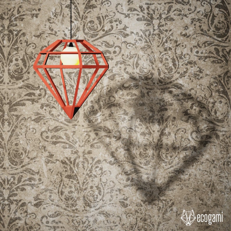 May include: A red diamond-shaped pendant light fixture hangs from a black cord against a patterned wall. The light casts a diamond-shaped shadow. The light fixture has a bulb inside. The logo "ecogami" is in the bottom right corner.