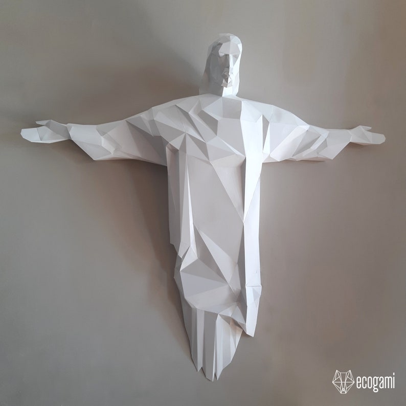 May include: A white paper sculpture of a person with outstretched arms, resembling the famous Christ the Redeemer statue in Rio de Janeiro, Brazil. The sculpture is made of folded paper and has a geometric, polygonal design.