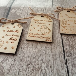May include: Three wooden Christmas gift tags with twine. The tags are decorated with a reindeer, an owl, and a bird. The tags are personalized with the names Amelia, Lillie-Mai, and Mabel. The tags also include the year 2019 and messages of love from Santa.