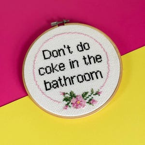 Könnte beinhalten: Ein weißer Stickrahmen mit dem Text "Don't do coke in the bathroom" und rosa Blumen.