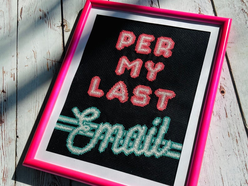 May include: A framed cross-stitch with a black background and pink frame. The cross-stitch reads "Per My Last Email" in a pixelated font. The words "Per My" are in pink and the word "Last" is in red. The words "Email" are in green.