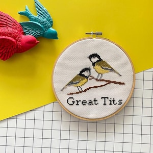 Op de afbeelding: Een witte borduurring met een kruissteekontwerp van twee gele vogels met zwarte koppen en bruine takken. De tekst "Great Tits" is onder de vogels geborduurd.