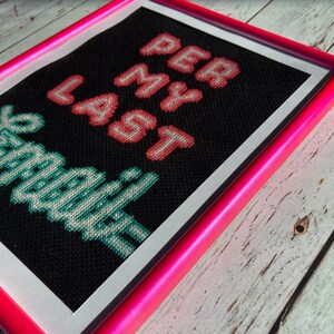 May include: Cross-stitch artwork framed in a bright pink frame. The artwork features the text "Get Off My Lawn" in green and "Per Lamer" in pink.
