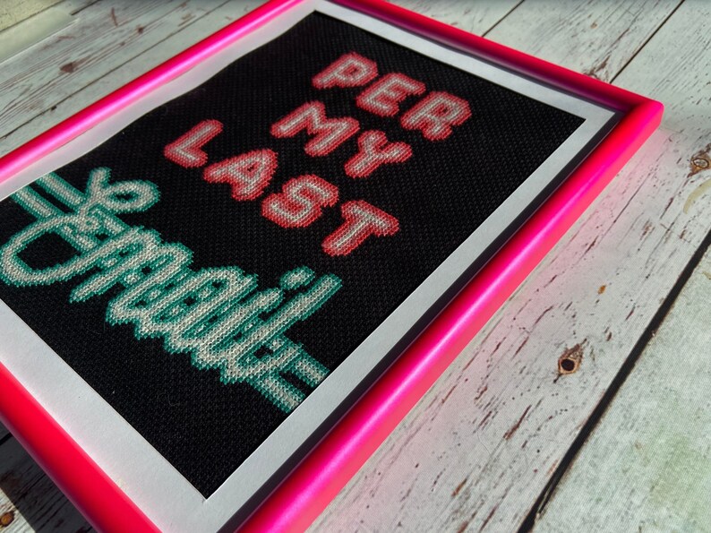 May include: Cross-stitch artwork framed in a bright pink frame. The artwork features the text "Get Off My Lawn" in green and "Per Lamer" in pink.