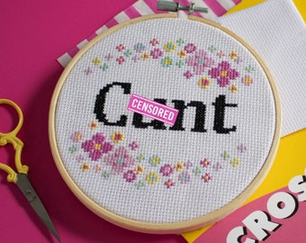 Könnte beinhalten: Ein weißer Stickrahmen mit einem schwarzen Kreuzstich-Design, das "Zensiert" sagt, umgeben von rosa, gelben und blauen Blumen.