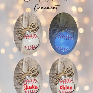 May include: Four white baseball-themed Christmas ornaments with red stitching. Two ornaments are plain, and two have names written on them: "Justin" and "Chloe".
