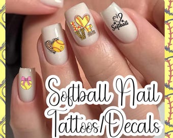 Op de afbeelding: Off-white vingernagels versierd met softball-thema nagelstickers. Ontwerpen omvatten een gele softball met een roze strik, een hartvormige softball met luipaardprint, het woord LOVE met softball-patronen en de tekst I love Softball.