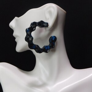 May include: Black and blue hoop earrings with a textured, abstract design. The earrings are made of resin and have a unique, modern look.