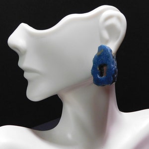 May include: A pair of blue and gold earrings with a unique, irregular shape. The earrings are made of ceramic and have a textured surface.