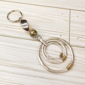 May include: Silver key chain with a decorative ring made of three concentric circles. The ring is attached to a silver and gold bead and a silver loop. The loop is attached to a silver key ring.
