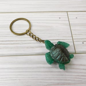 May include: A green sea turtle keychain with a bronze key ring and chain. The turtle is made of resin and has a detailed shell.