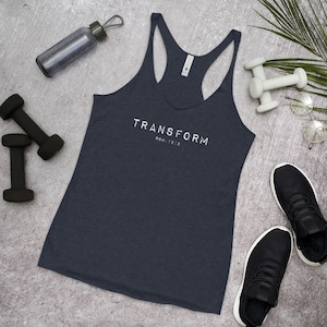 Könnte beinhalten: Ein marineblaues Tanktop mit dem weißen Aufdruck "TRANSFORM". Der Text "ROM. 12:2" steht unter dem Wort "TRANSFORM". Das Tanktop ist von Fitnessgeräten umgeben, darunter Kurzhanteln, eine Wasserflasche und Turnschuhe.