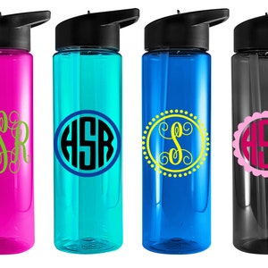 May include: Four reusable water bottles with different colored lids and bodies. Each bottle has a different monogram design on the front. The monograms are in different colors and styles. The bottles are all clear and have a straw.